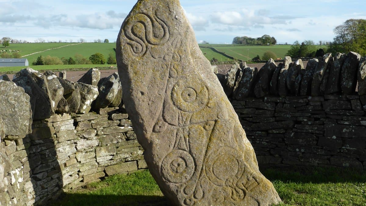 Weathered carved upright stone beside a grassy roadside.