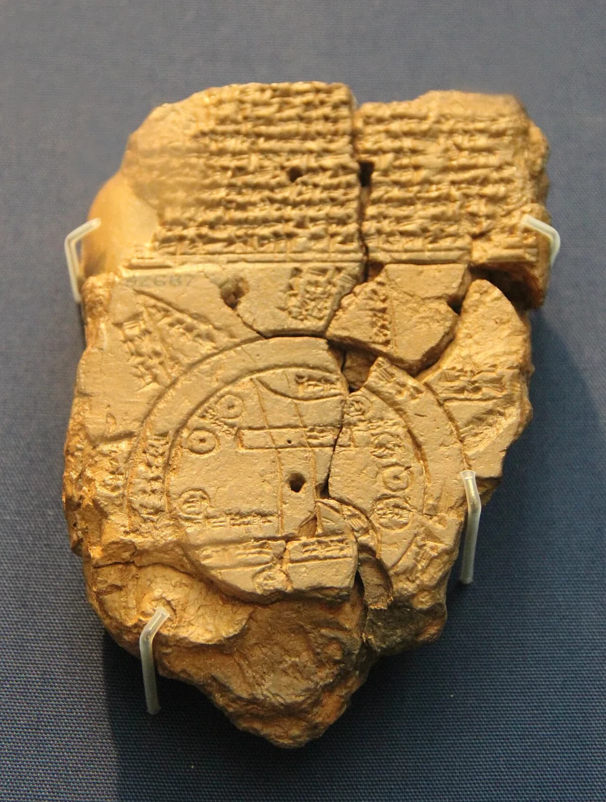 Broken clay tablet with cuneiform writing above a circular map.