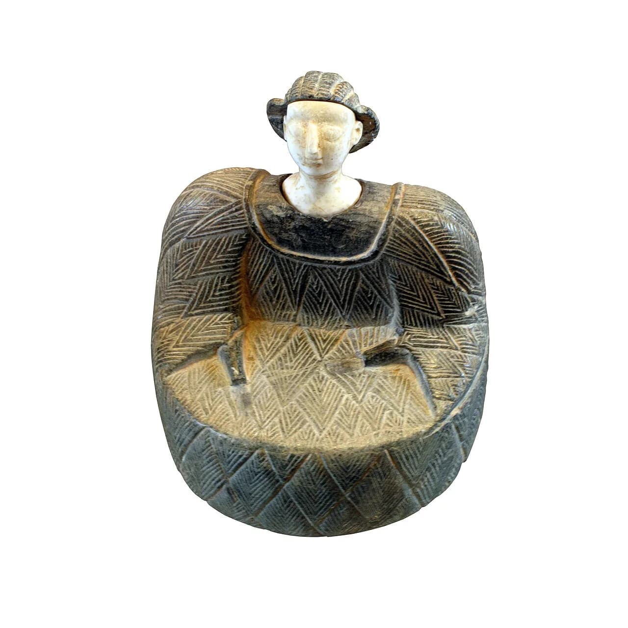 Seated Bactrian figurine with a pale stone head and a dark garment carved with a herringbone pattern.