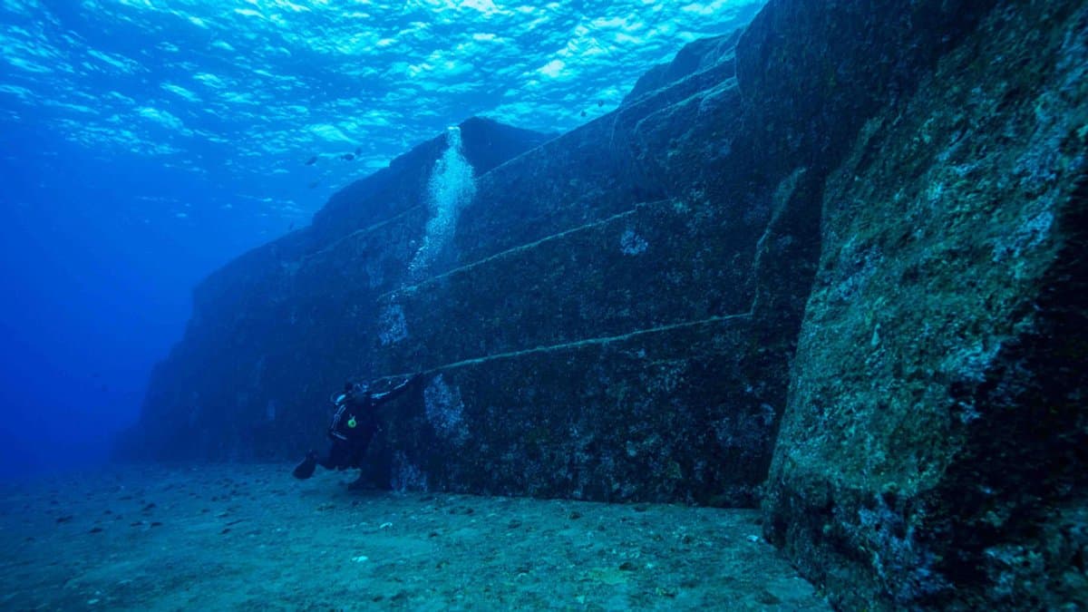 Diver beside broad, angular underwater stone terraces.