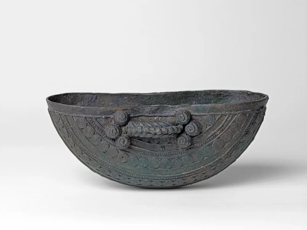 Crescent-shaped bronze bowl from Igbo-Ukwu with a twisted handle, raised bosses and rows of spirals.
