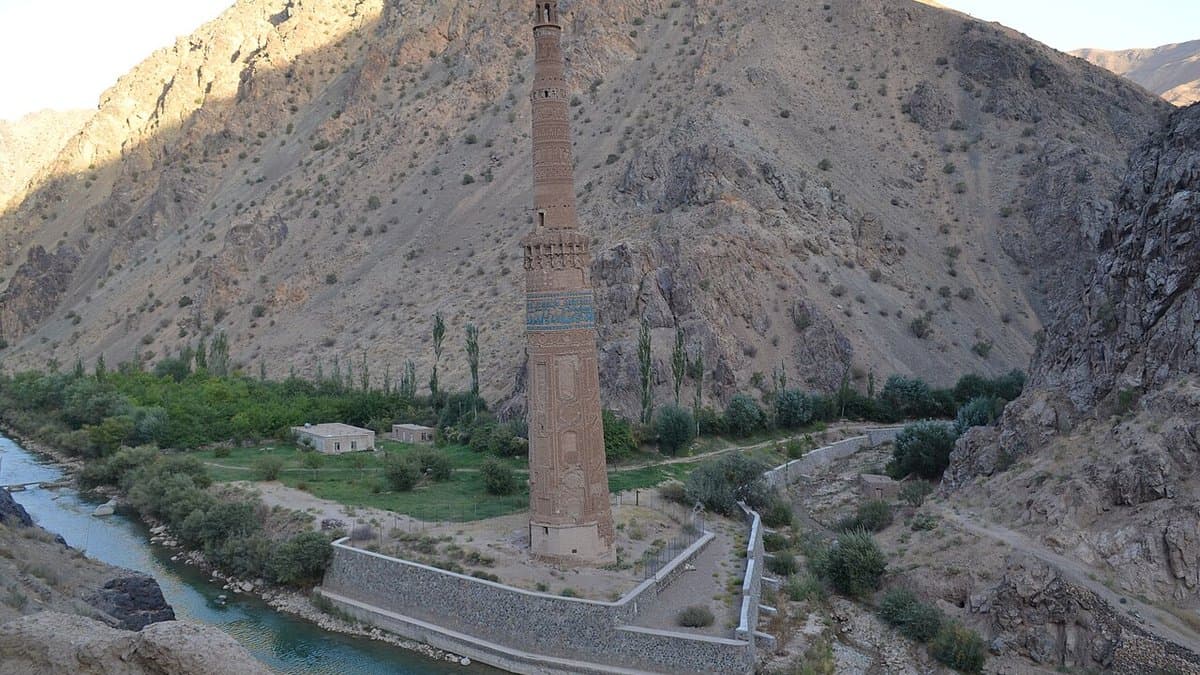Tall decorated brick minaret rising beside a river in the Jam valley.