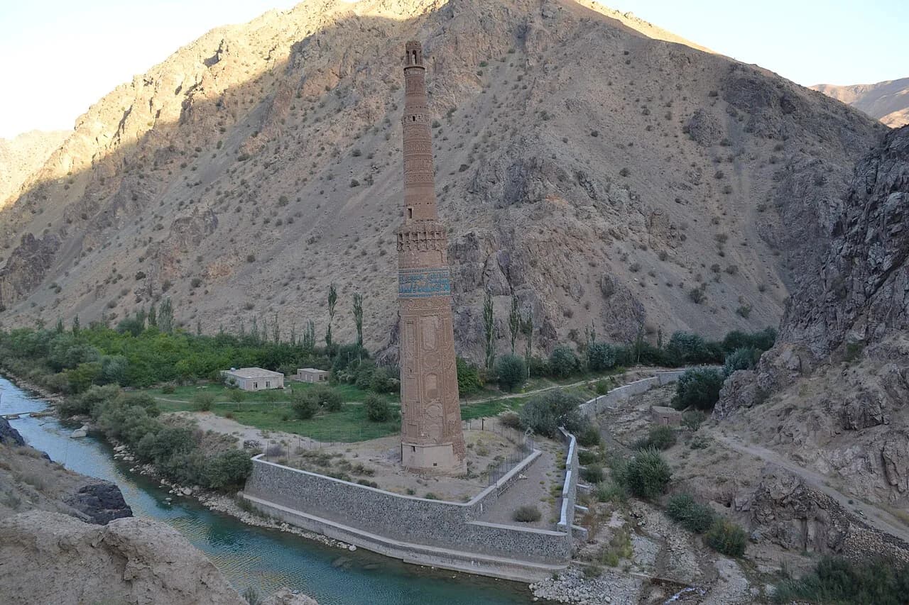 Tall decorated brick minaret rising beside a river in the Jam valley.