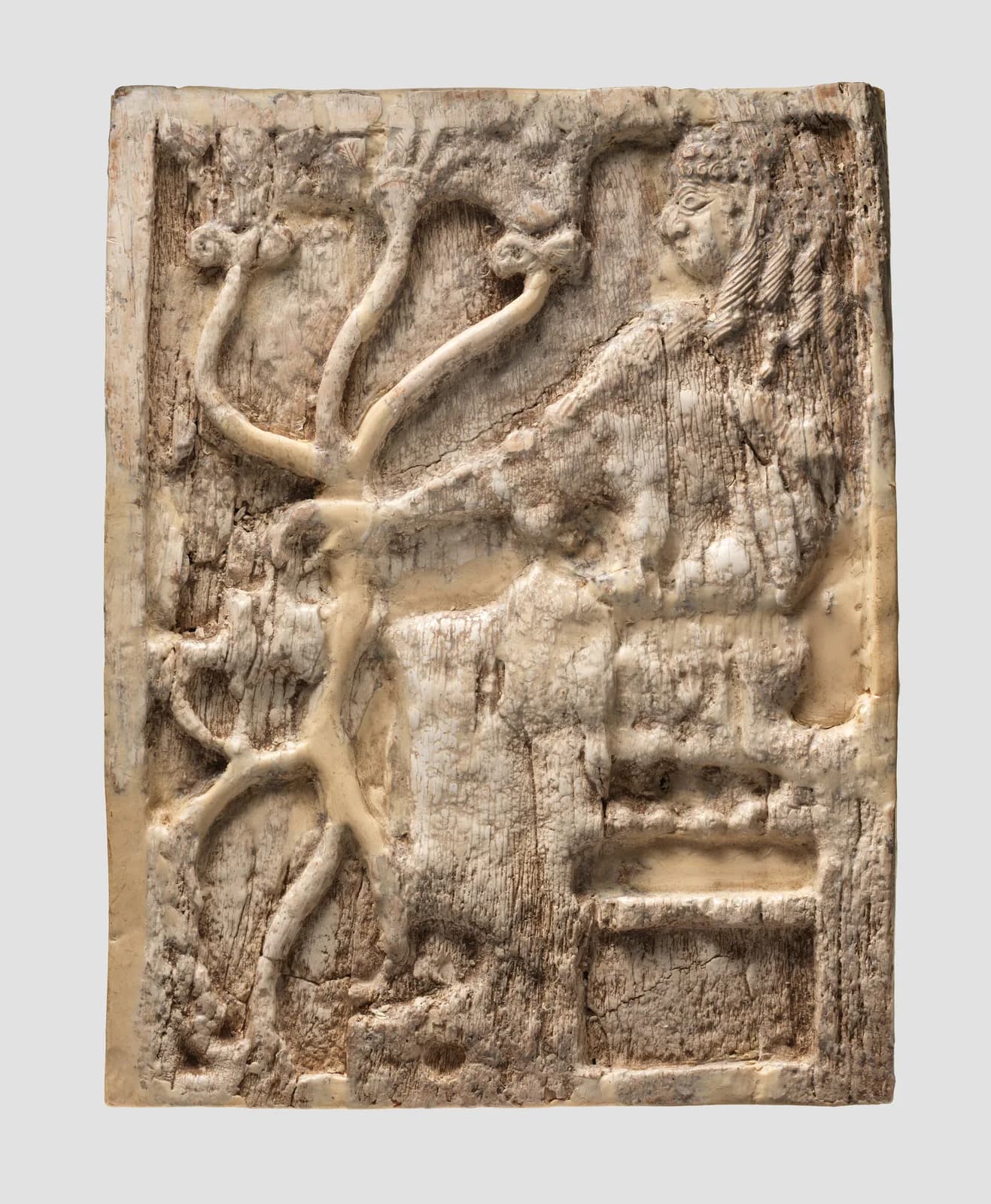 Worn ivory panel carved with a seated woman holding a stalk that curls into tendrils.