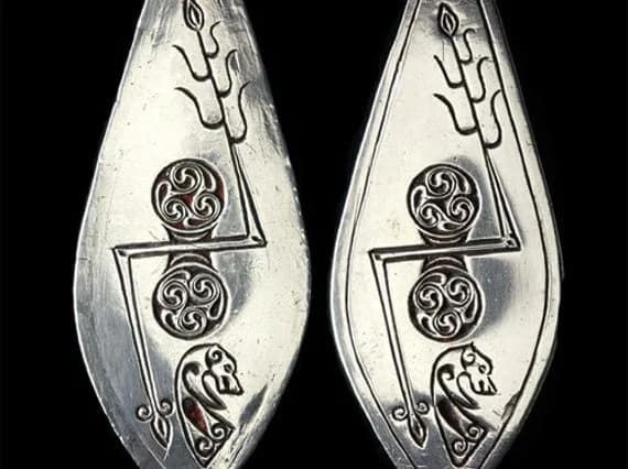 Two similar leaf-shaped silver plaques with Pictish symbols displayed side by side.