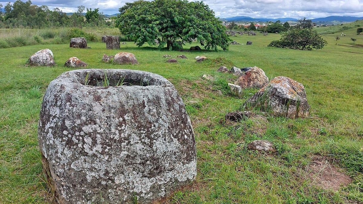 Large carved stone jars standing across a grassy area at Plain of Jars Site 1.