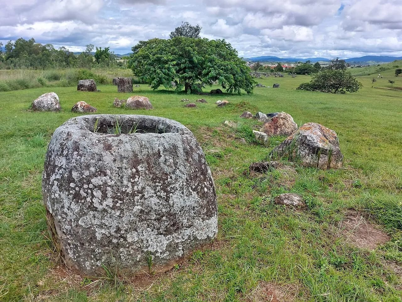 Large carved stone jars standing across a grassy area at Plain of Jars Site 1.