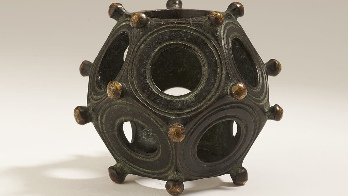 Hollow bronze object with pentagonal faces, circular openings, and corner knobs.