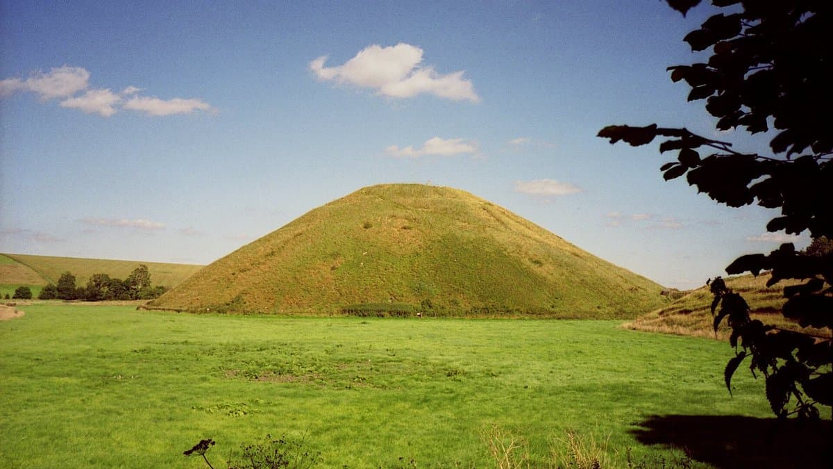 Large grass-covered conical mound rising above fields.