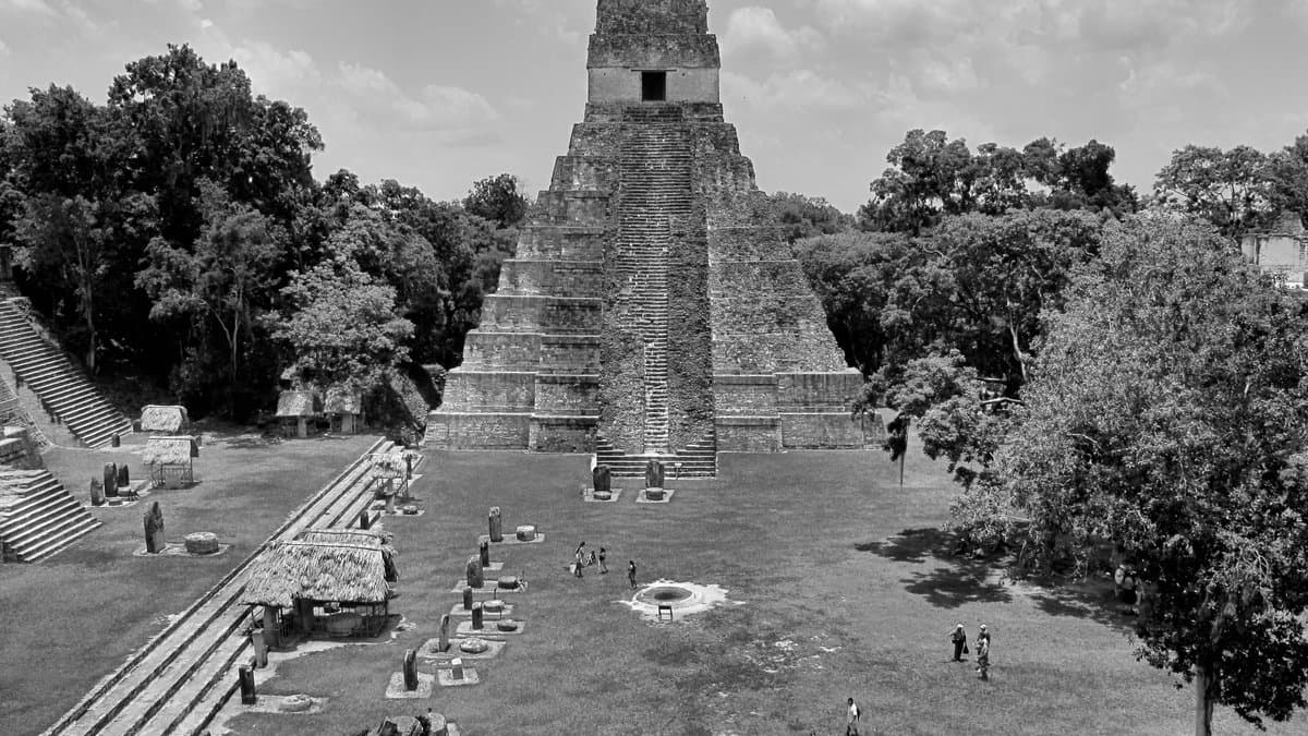 Black-and-white view across Tikal's Great Plaza toward a steep stone temple.