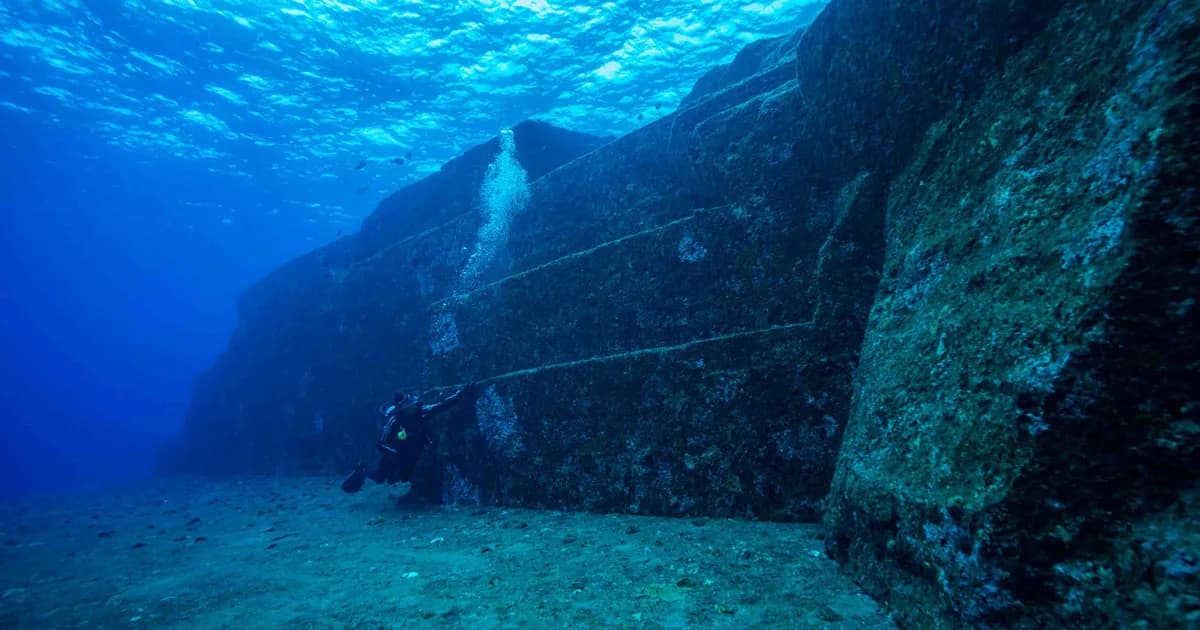 Diver beside broad, angular underwater stone terraces.