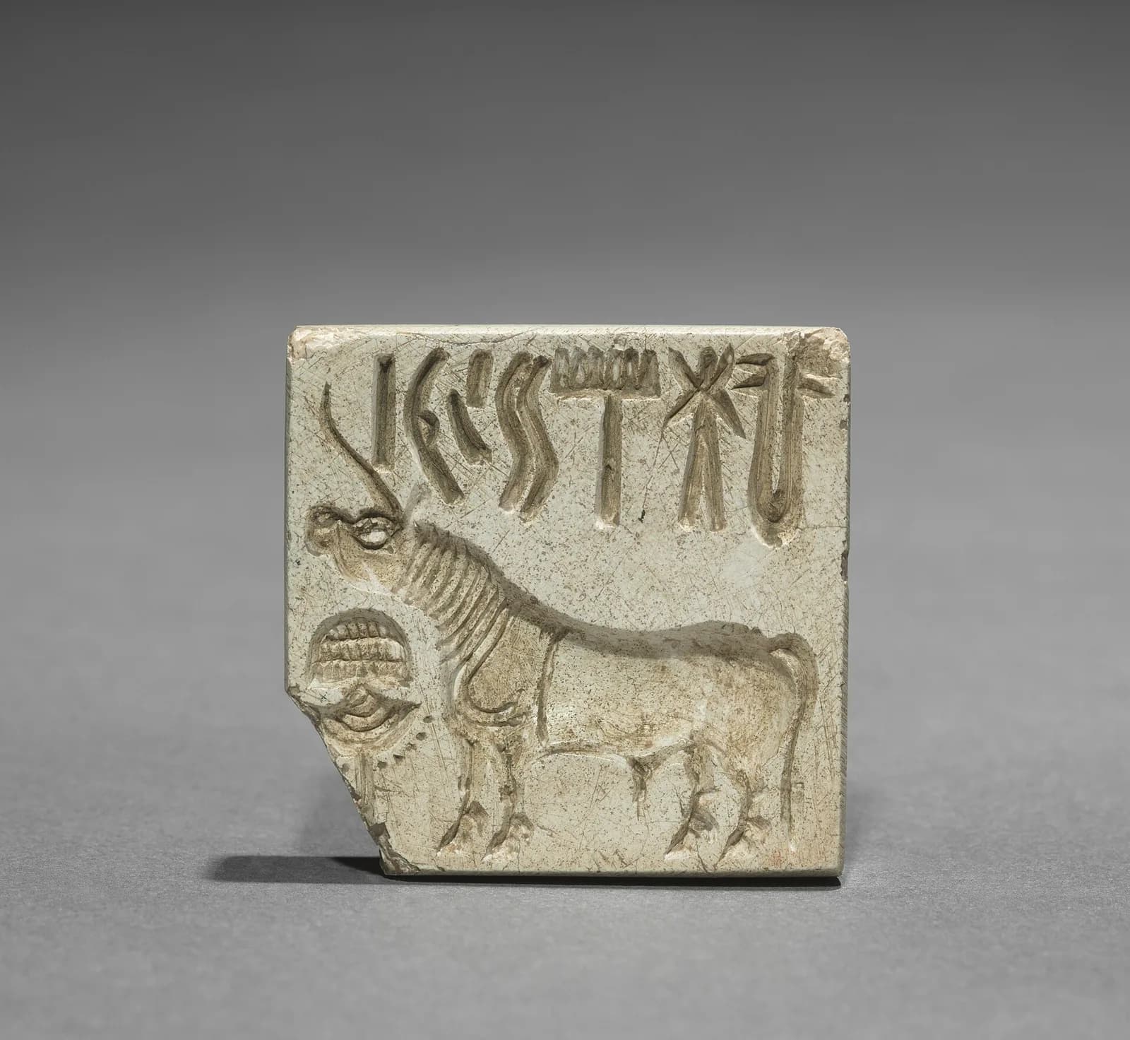 Small square carved seal with a row of signs above a one-horned animal.