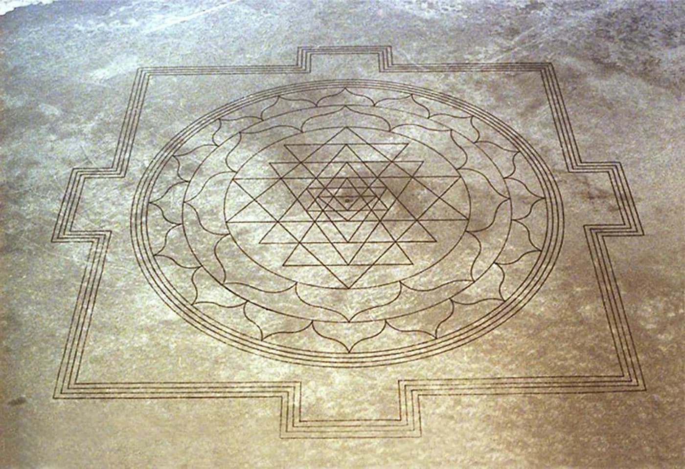 Large Sri Yantra pattern carved into pale desert ground, seen from above.