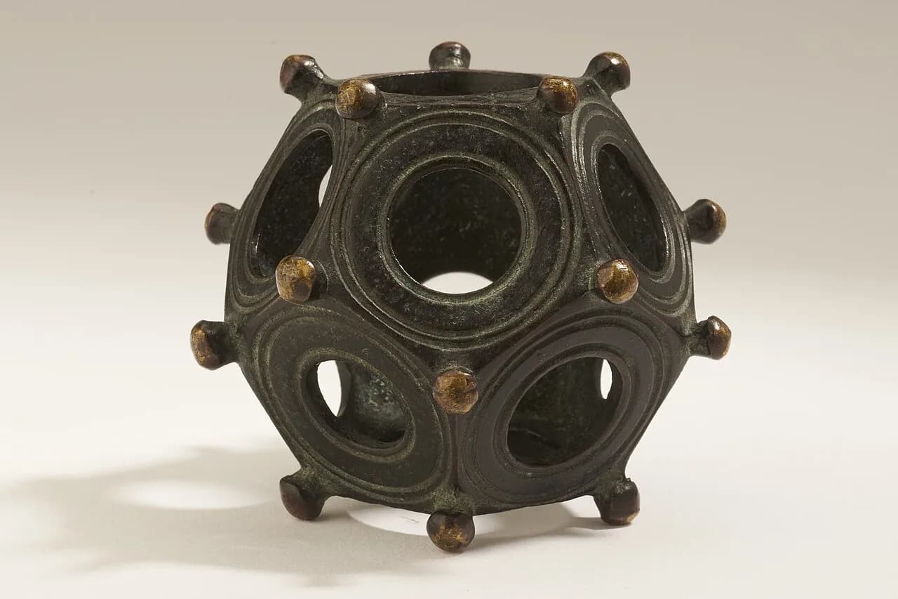 Hollow bronze object with pentagonal faces, circular openings, and corner knobs.
