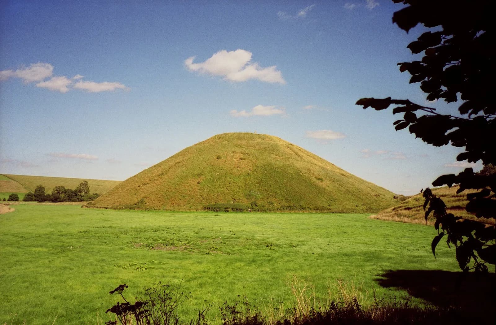 Large grass-covered conical mound rising above fields.