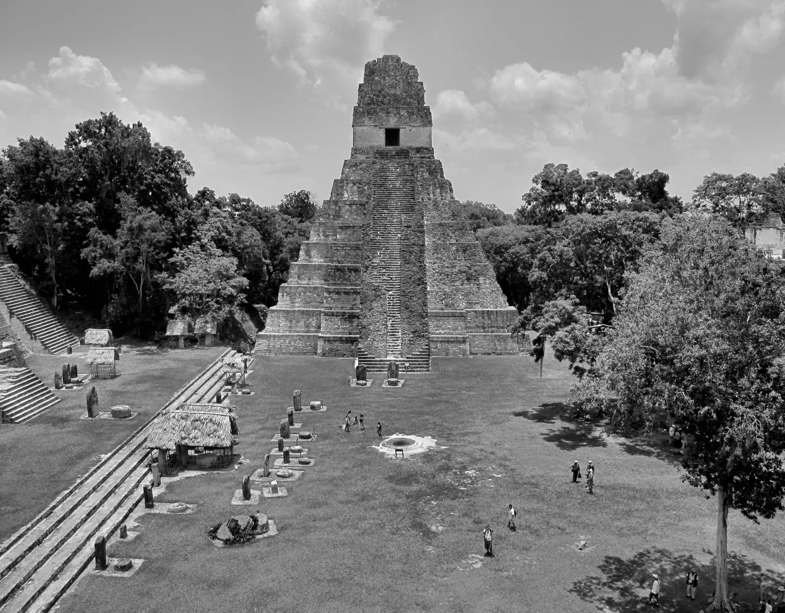 Black-and-white view across Tikal's Great Plaza toward a steep stone temple.